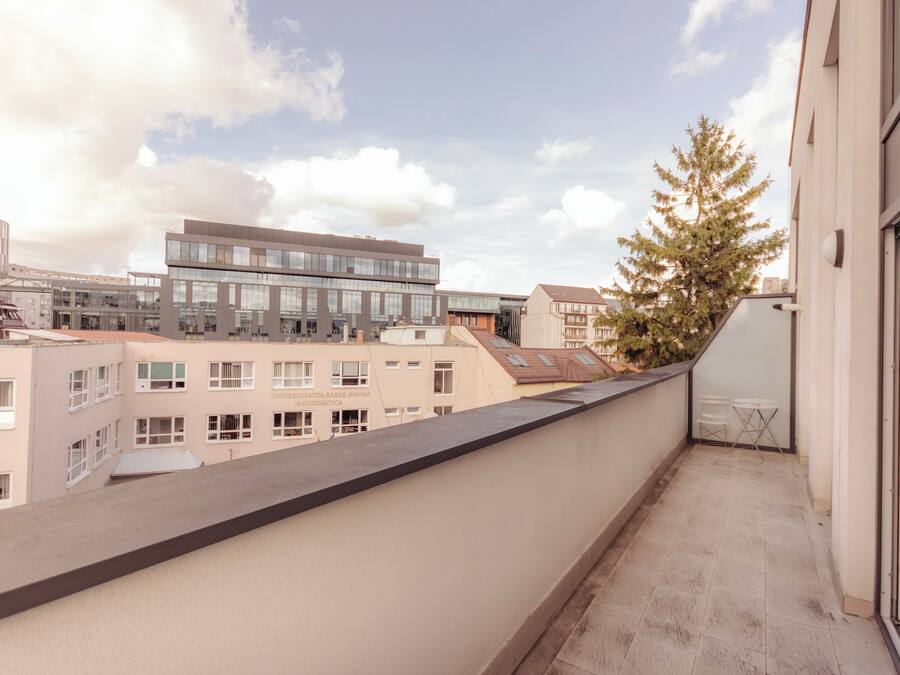 A balcony with a view of modern buildings and a tree.