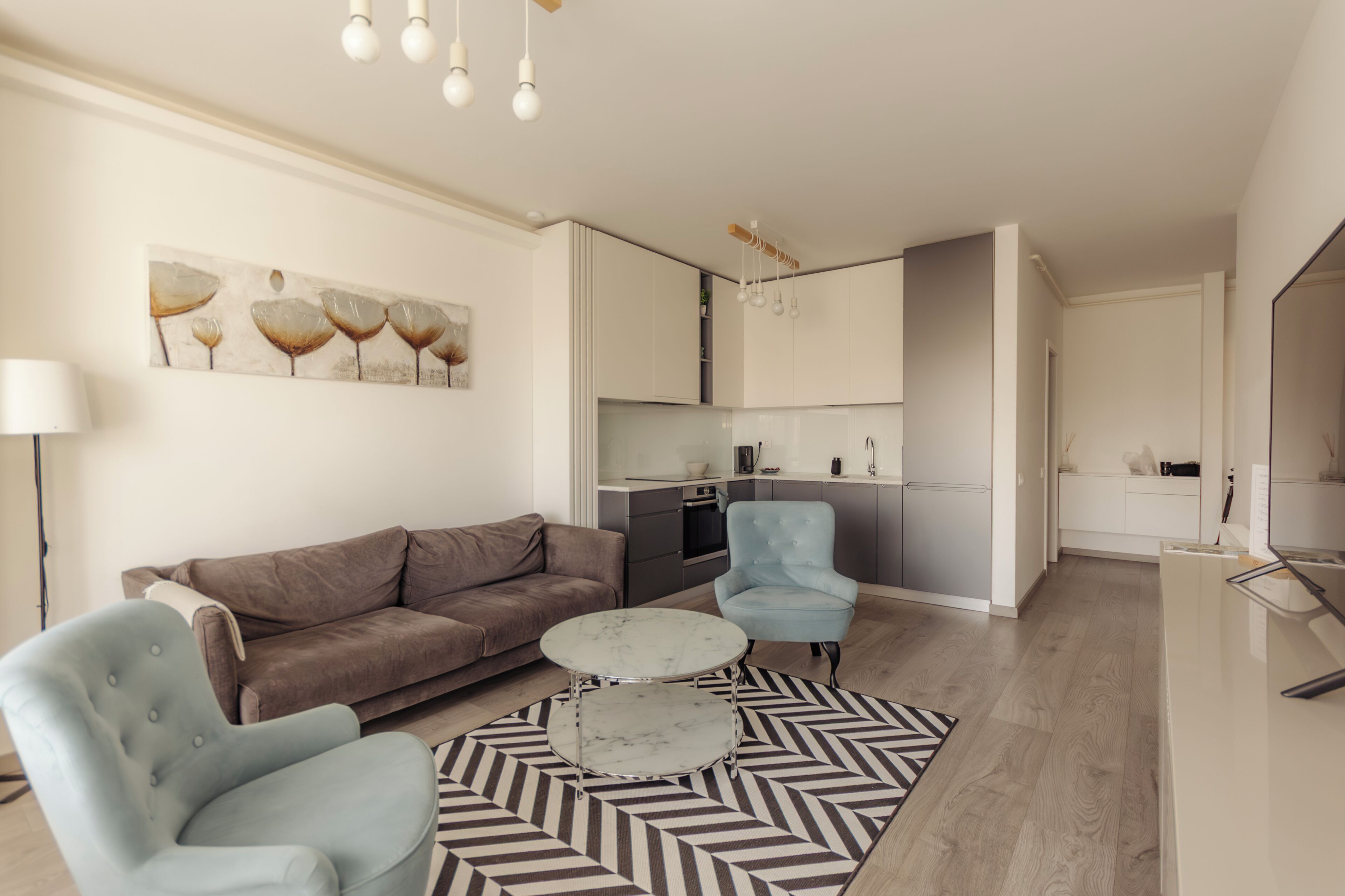 Un salon moderne comprenant un canapé, un fauteuil et une table basse, ainsi qu’un coin cuisine et une table à manger.