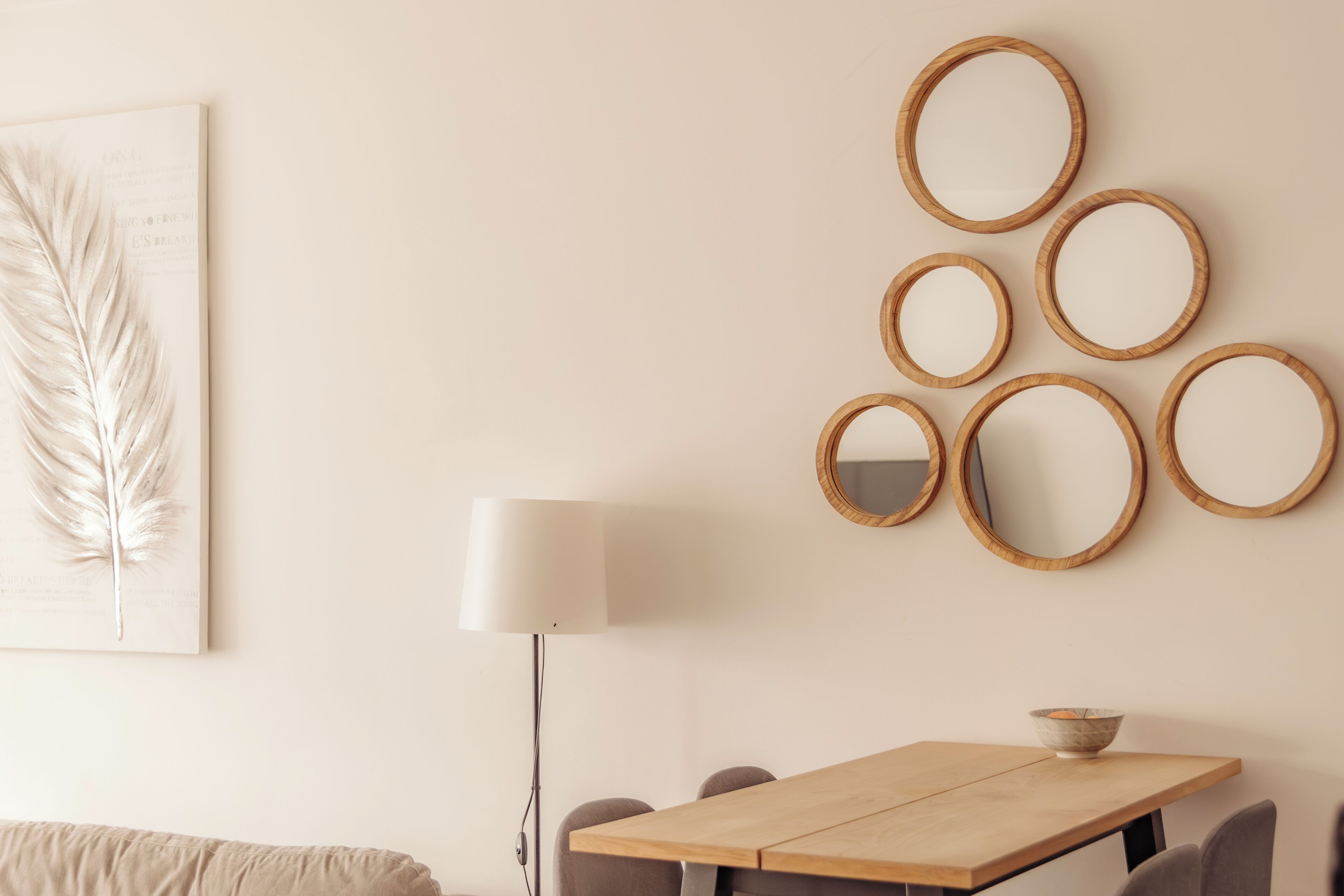 A dining area with a wooden table, six wall-mounted mirrors, a floor lamp, and a framed feather artwork.