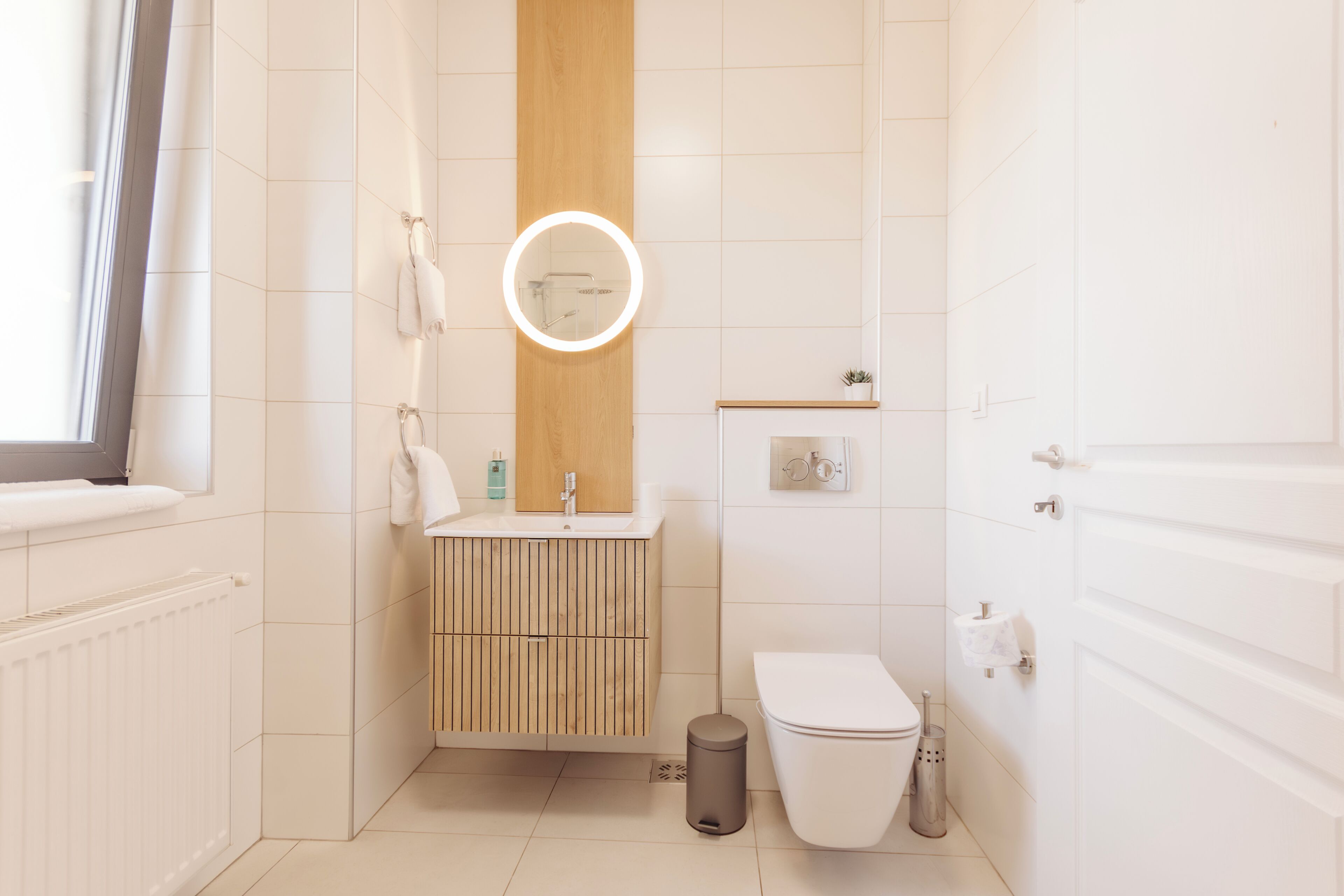 A modern bathroom with a wooden vanity, a toilet, a sink with a mirror, and a window.