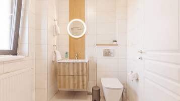 A modern bathroom with a wooden vanity, a toilet, a sink with a mirror, and a window.