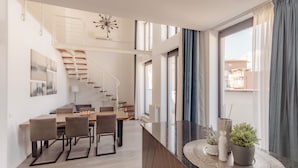 Un interior moderno con zona de comedor, escalera y ventanas amplias.
