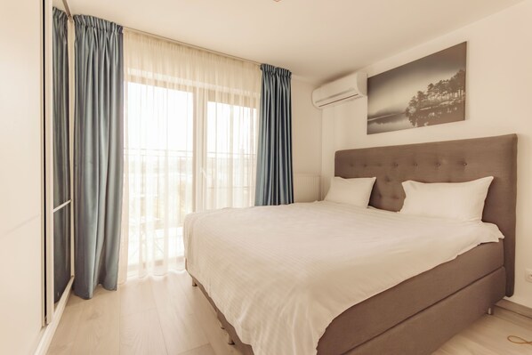 Un dormitorio con una cama grande, una ventana con cortinas, un aire acondicionado de pared y un cuadro.