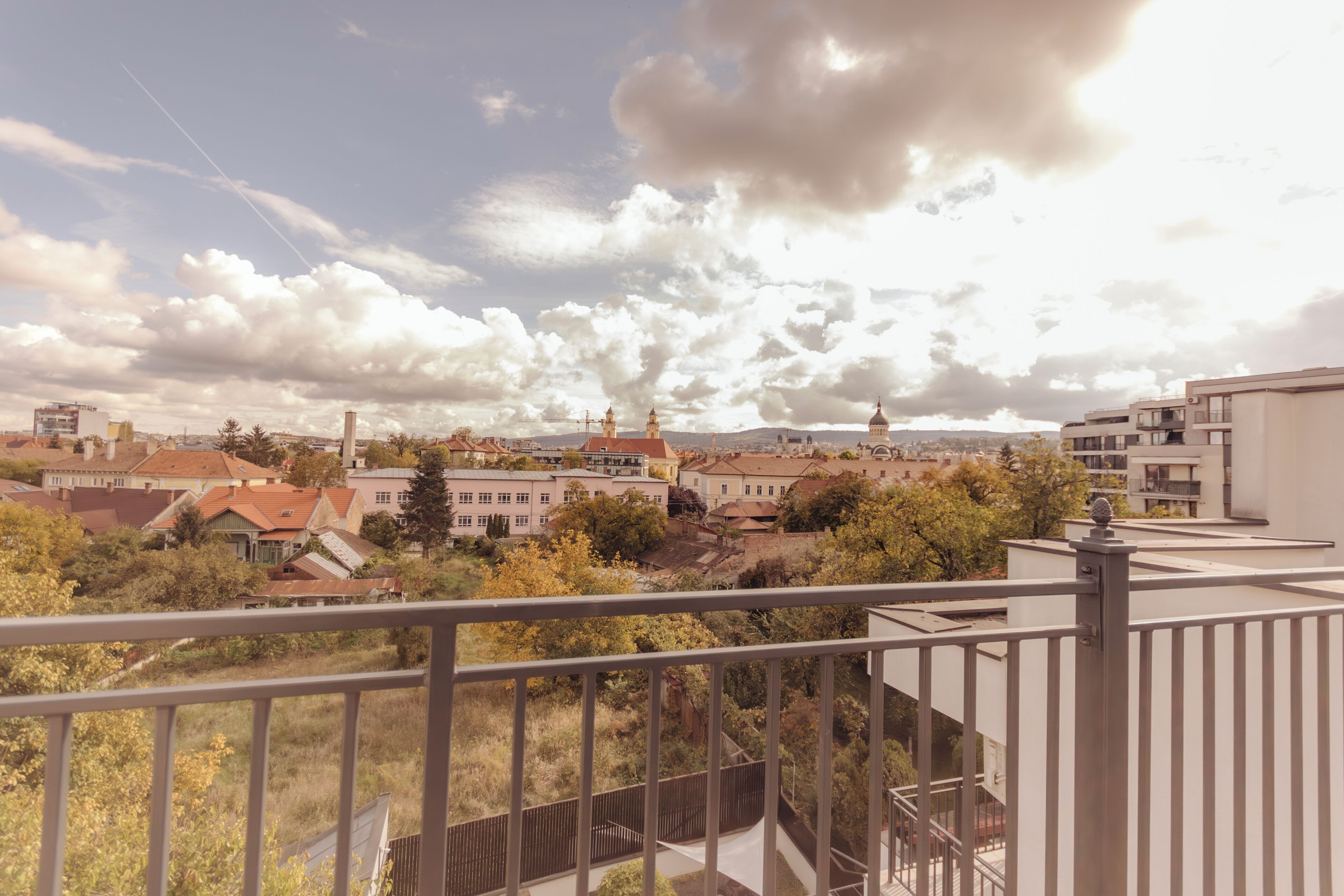 A balcony with a view of a cityscape, including buildings and trees.