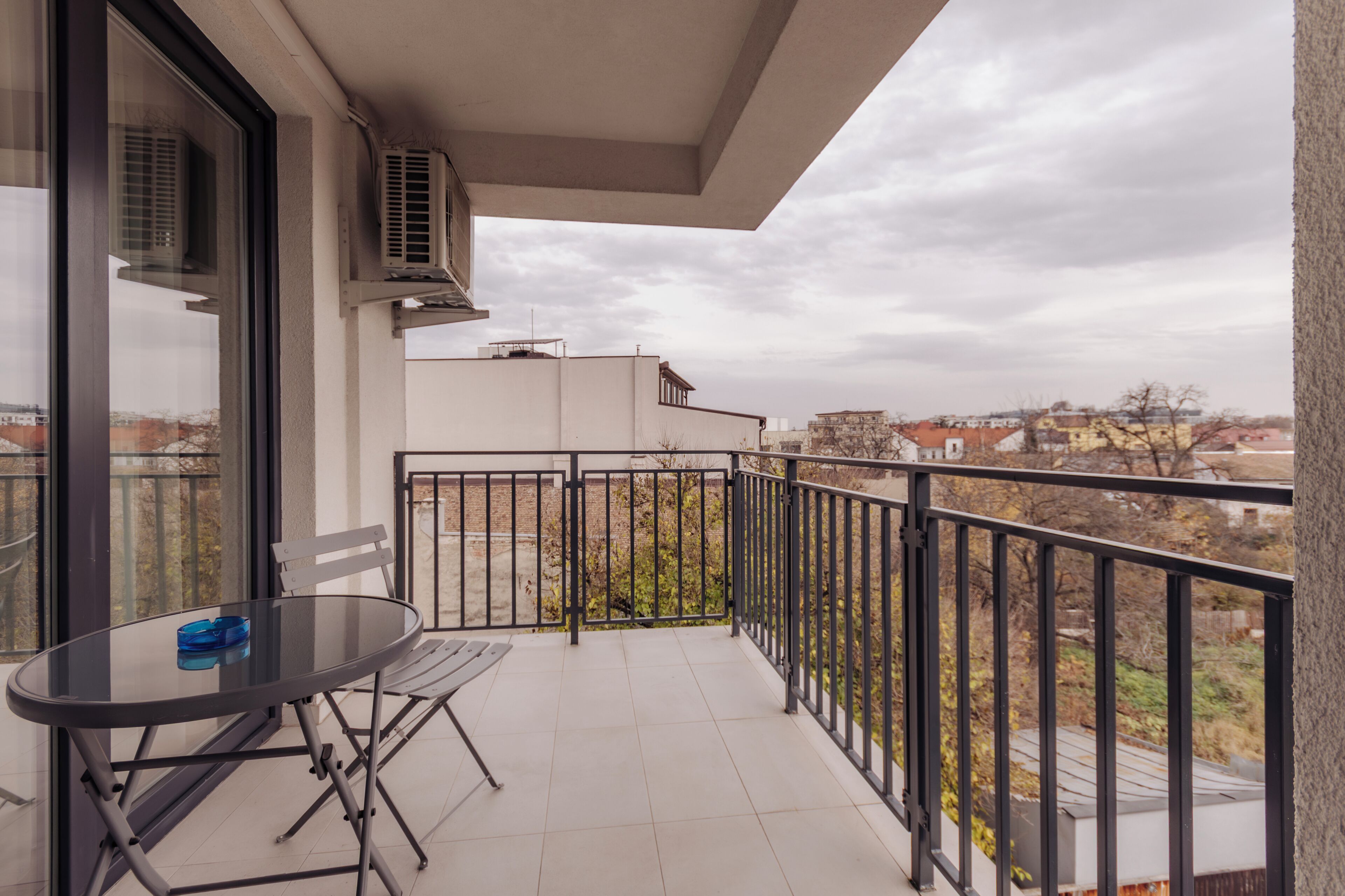 En balkon med bord og stole, klimaanlæg og udsigt til bygninger.