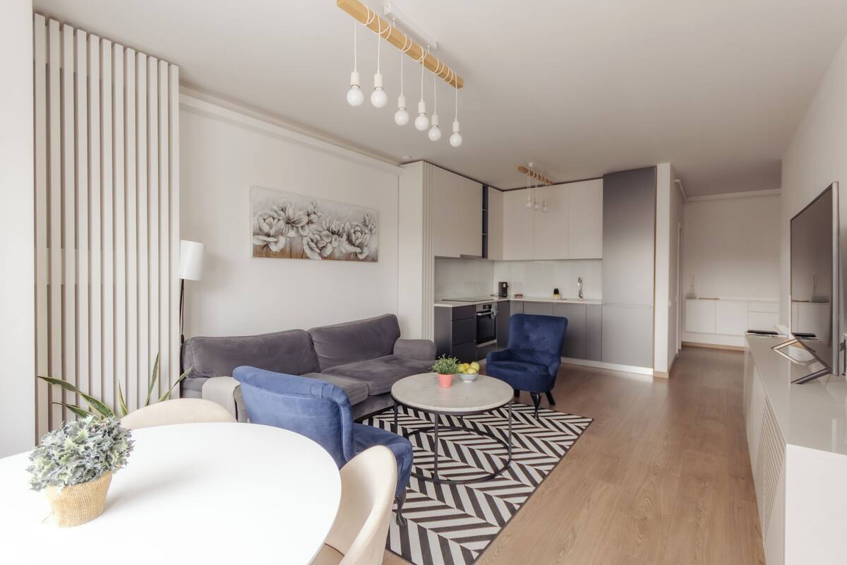 Una sala moderna con un sofá, sillas, una mesita de centro y una cocina al fondo.