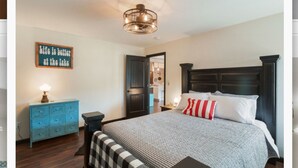 A bedroom with a bed, a dresser, a nightstand, a wall-mounted lamp, and a door leading to another room. - Lakefront duplex property, nicely finished. 2 bedroom and queen size hide-a-bed. (Divide)