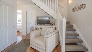Una escalera con un letrero que dice "Beach House", una puerta blanca, un sillón color arena y un televisor de pantalla plana sobre un mueble.