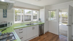Una cocina moderna con armarios blancos, encimera verde, microondas integrado, estufa y lavavajillas. Hay una ventana con vista a una cerca de madera y una puerta que da a una terraza.