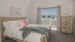 Un dormitorio con cama de madera, mesita de noche, cómoda y balcón con vista a una casa.