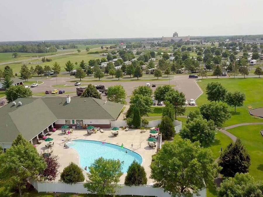 A large swimming pool with lounge chairs and umbrellas, surrounded by a parking area and a building with a green roof.