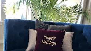 Un canapé bleu avec un coussin portant l’inscription « Joyeuses fêtes » et deux autres coussins.