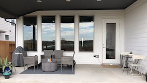Une terrasse couverte, aménagée avec des meubles en osier, un barbecue et des plantes en pot.