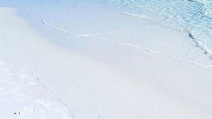 Een strand met helderblauw water en wit zand.