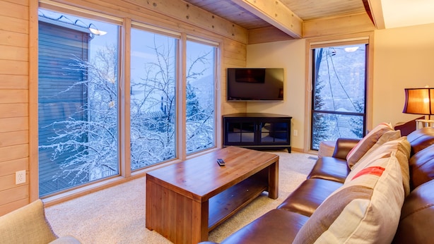 A cozy living room with a wooden coffee table, leather sofa, and large windows offering a view of a snowy landscape. - 6 Bedroom + 2 Den Duplex 2 Blocks from PC Mountain! Can't beat this place! (Park City)