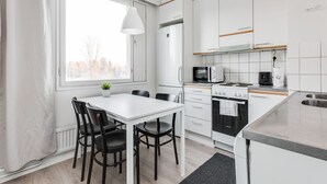 Una cocina moderna con armarios blancos, una mesa de comedor con sillas, un ventanal y vistas a árboles.