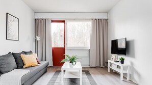 Una sala de estar moderna con un sofá gris, una mesa de centro blanca, una puerta roja y un ventanal con cortinas.