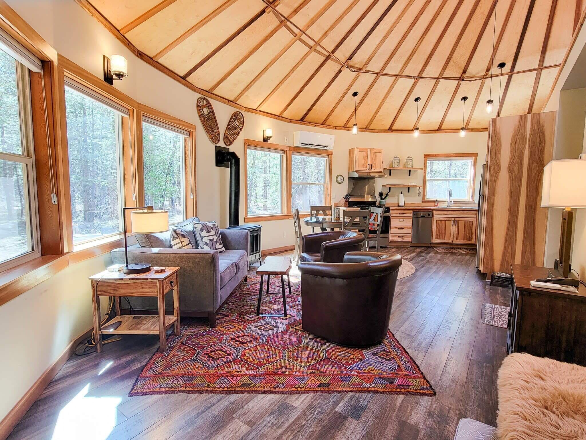 Un interior acogedor con techo de madera, ventanas amplias, un sofá, una mesa de comedor y una zona de cocina.