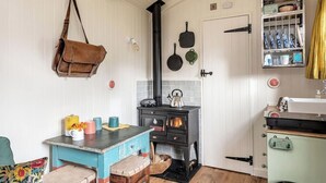 A cozy kitchen with a wooden table, chairs, a stove, and a hanging bag. - Beautiful hut in countryside garden with wood fired hot tub near Bath & Frome (Wingfield)