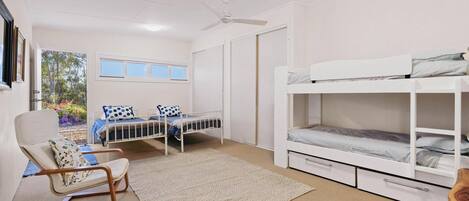 Une chambre avec deux lits, une chaise, un ventilateur de plafond et une fenêtre.