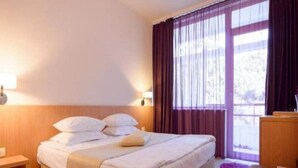 A hotel room with a large bed, a desk, and a window with curtains. - Sara (Neptun)