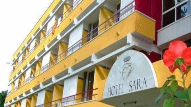 A multi-story hotel with balconies, a sign reading "HOTEL SARA," and a large red flower decoration. - Sara (Neptun)