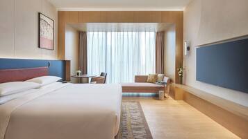 A modern hotel room with a large bed, a sofa, a small table, and a TV.