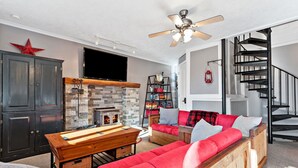 A living room with a fireplace, a wooden coffee table, a red sofa, and a black spiral staircase.