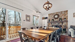 A dining area with a wooden table and metal chairs, a stone wall with a clock, and a view through large glass doors.