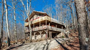 A multi-story wooden cabin with a balcony, surrounded by trees.