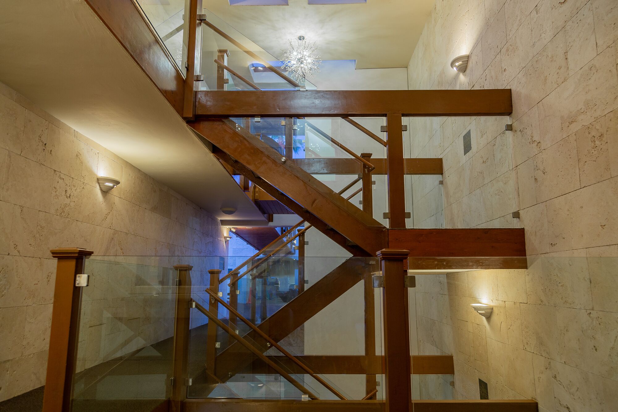A modern interior with a wooden staircase, glass railings, and stone walls.