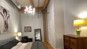 Une chambre à coucher avec un lit, une commode en bois, un lustre, une chaise et un miroir.