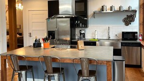 Une cuisine moderne dotée d’un îlot central, d’appareils électroménagers en acier inoxydable et de tabourets de bar.