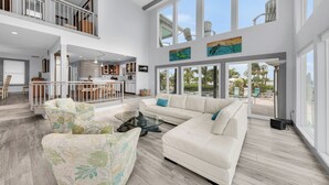 A spacious living area with a large sectional sofa, a glass coffee table, and a view of the outdoors through large windows.