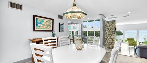 A modern dining area with a white table and chairs, a hanging light fixture, and a view of the ocean through large windows.