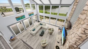 A spacious living area with a large window overlooking a river, furnished with a sectional sofa, armchairs, and a flat-screen TV.