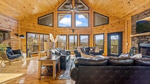 Interior espacioso de una cabaña de madera con techo alto, ventanas amplias, chimenea y una zona de estar acogedora.