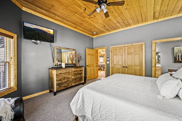 A bedroom with a large bed, wooden ceiling, a dresser, a TV, and a mirror. - StunningViews,HotTub,Fireplace,Theater,Arcade (Sevierville)