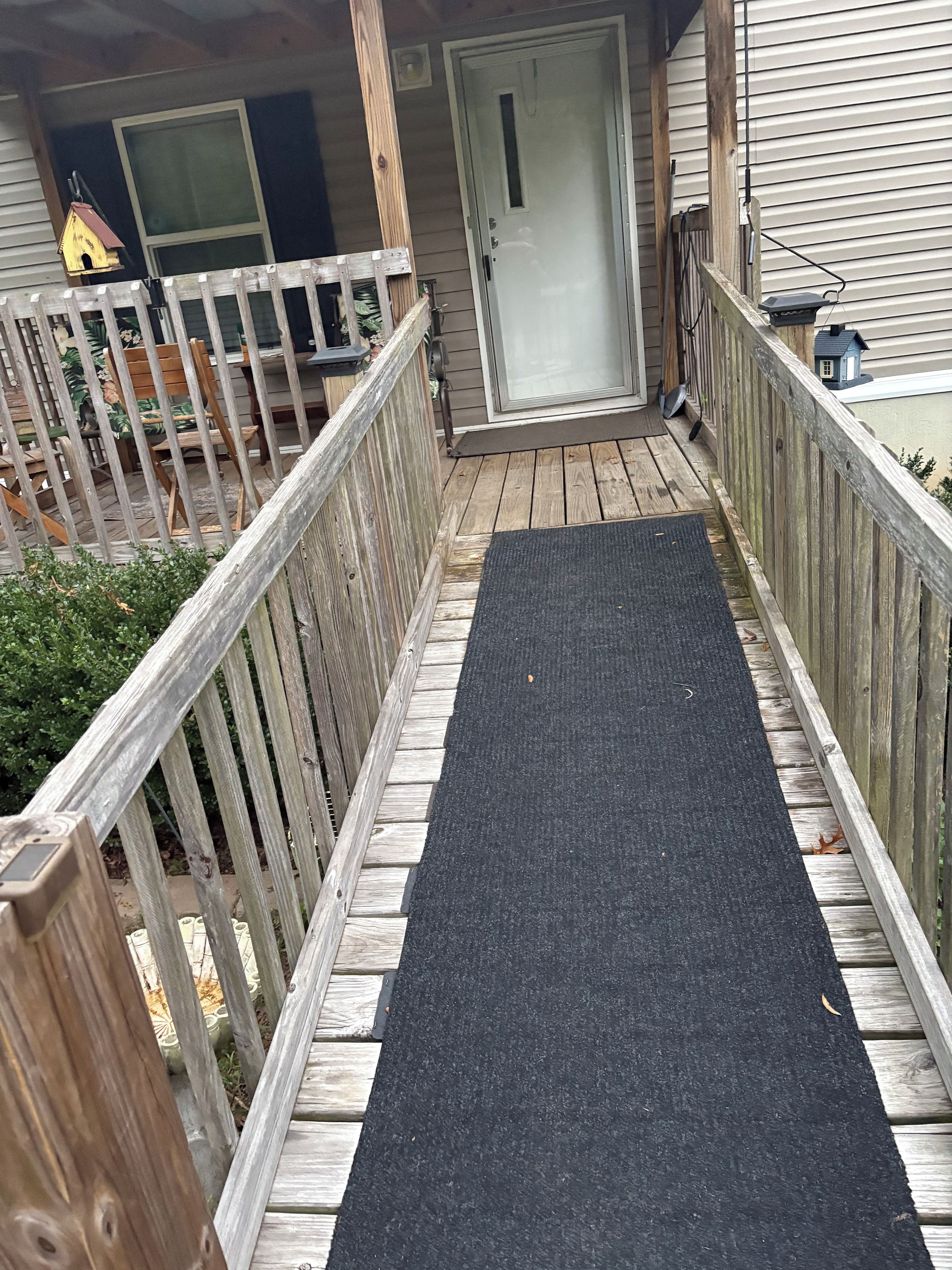 A wooden deck with a black mat leading to a door.