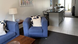 A modern living room with a sofa and a coffee table, a kitchen with a bar area, and a dining area with a table and chairs. - Townhouse Near City Centre, River & Stadium (Waikato)