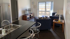A modern kitchen with a stainless steel refrigerator, a bar area with stools, a dining table, and a large window offering a view of the backyard. - Townhouse Near City Centre, River & Stadium (Waikato)