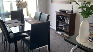 A dining area with a table and chairs, a vase with flowers, and a bookshelf with glasses. - Townhouse Near City Centre, River & Stadium (Waikato)