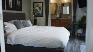 Une chambre d’hôtel moderne avec un grand lit, une salle de bain dotée d’un miroir et d’un lavabo, et des œuvres d’art accrochées aux murs.
