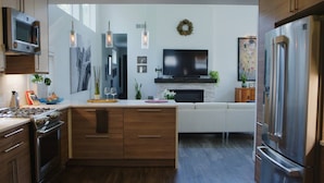 Une cuisine moderne avec des meubles en bois, un îlot central, un four encastré et un réfrigérateur en acier inoxydable.