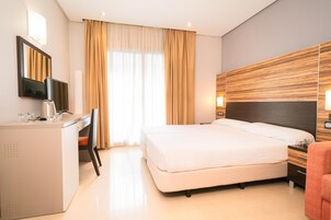 Une chambre d’hôtel avec un lit, un bureau, une chaise, une télévision et une tête de lit en bois.