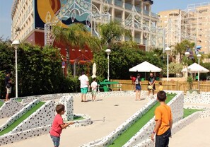 Une cour avec une fontaine, des palmiers et un bâtiment dont le mur arrière est orné d’une fresque colorée.