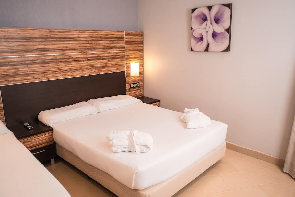 A hotel room with a large bed, a nightstand with a lamp, and a wall-mounted artwork.