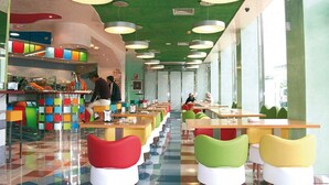 A cafeteria with colorful chairs and tables, a counter with food items, and a green ceiling. - Magic INN (Oropesa del Mar)