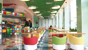 A cafeteria with colorful chairs and tables, a counter with food items, and a green ceiling. - Magic INN (Oropesa del Mar)