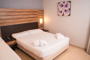 A hotel room with a large bed, a nightstand with a lamp, and a wall-mounted artwork.
